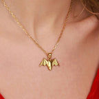 Gold necklace with a bat-shaped pendant on a person wearing a red top.