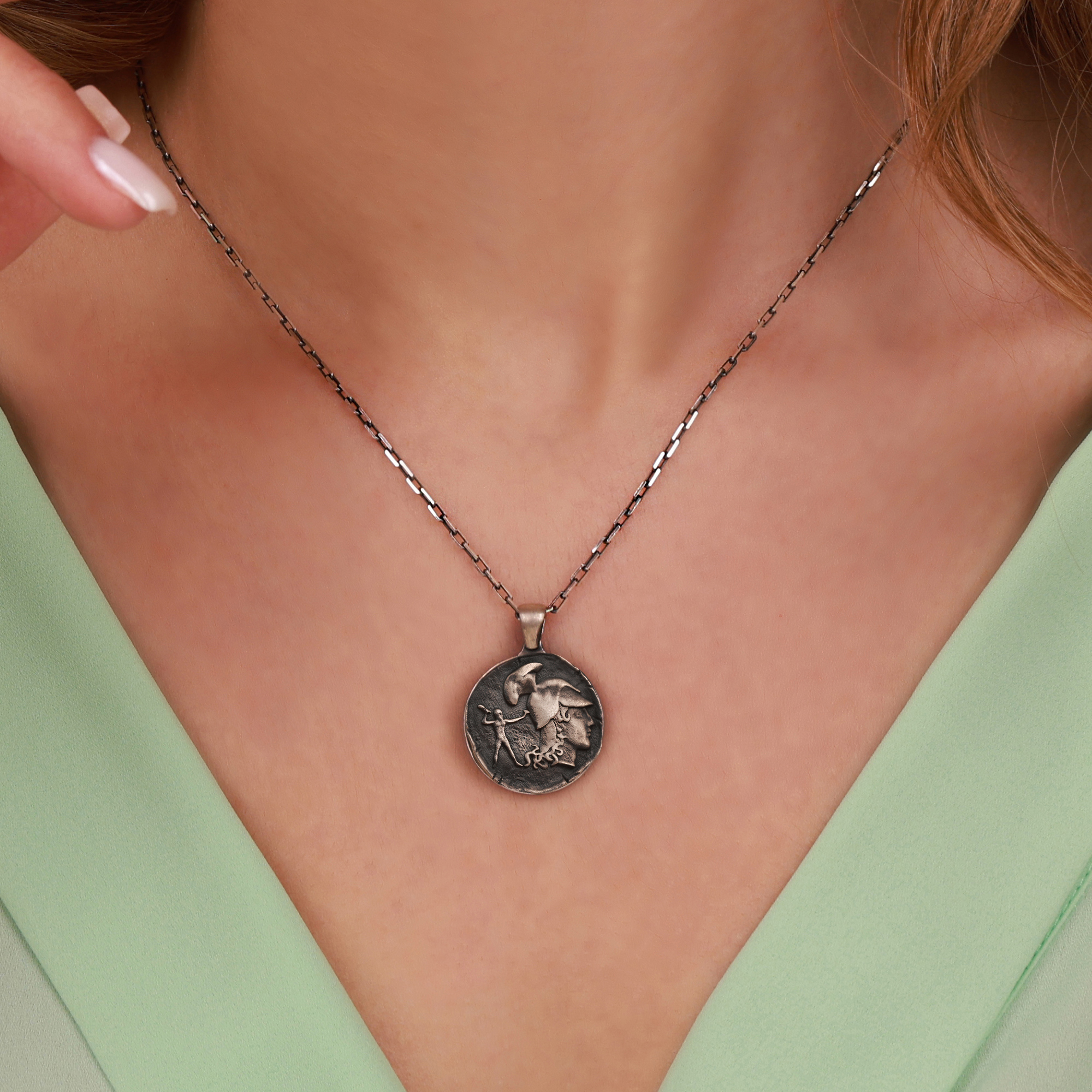 Necklace with an athena coin pendant worn by a person against a neutral background