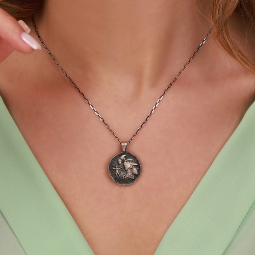 Necklace with an athena coin pendant worn by a person against a neutral background