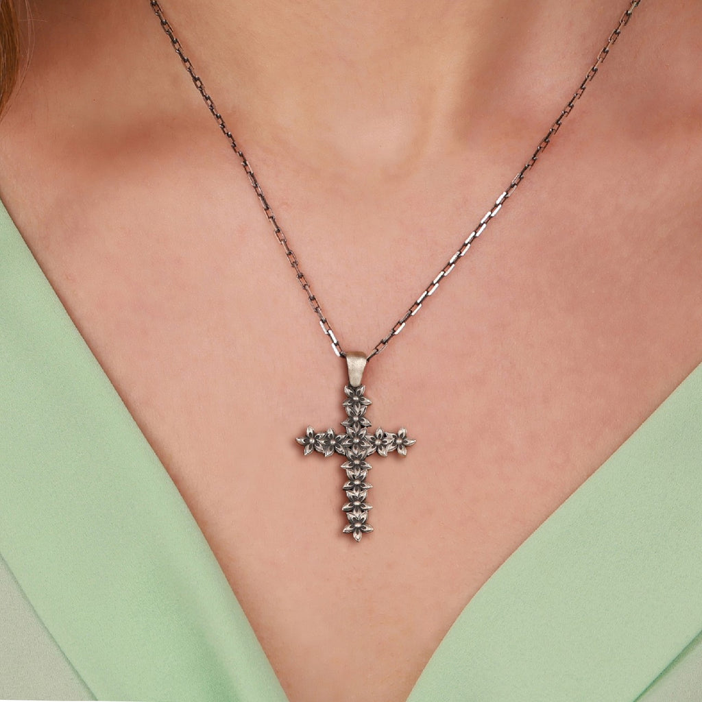 An oxidized sterling silver floral cross pendant necklace on a person wearing a green top