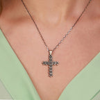An oxidized sterling silver floral cross pendant necklace on a person wearing a green top
