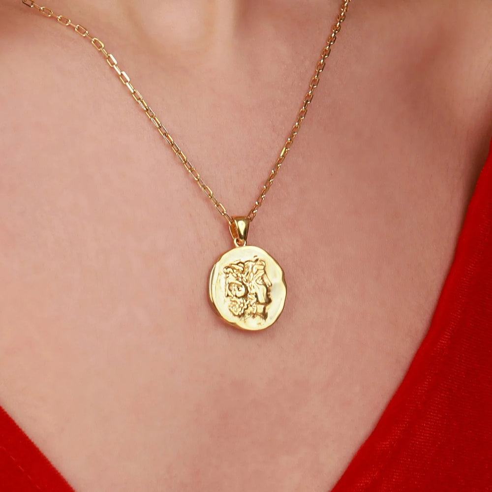 A gold coin pendant necklace featuring an embossed lion head, worn on a model's neck over a red top.