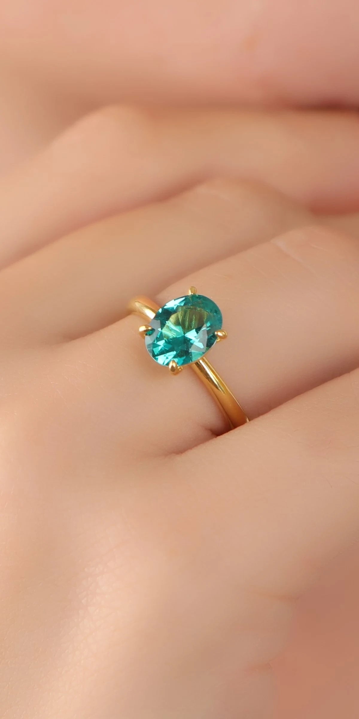 A gold ring with a round-cut turquoise gemstone worn on a person's finger, shown in a close-up shot.