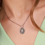 Necklace with a Virgin Mary pendant worn by a person against a neutral background
