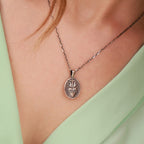 Silver necklace with a sacred heart pendant on a person wearing a light green top.