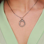 Silver necklace with a circular pendant worn by a person in a light green top.