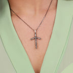 A sterling silver cross necklace on a person wearing a light green top