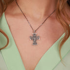 A close-up of a person wearing a silver-toned cross pendant necklace with a st michael the Archangel design, paired with a mint green top.