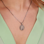 Silver necklace with a virgin mary pendant worn by a person against a light green background