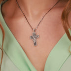 A close-up of a silver cross pendant necklace worn on a model's neck, featuring an embossed figure of Jesus Christ and the word 'INRI' on the cross, styled with a mint green top.