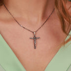 A close-up of a person wearing an oxidized sterling silver crucifix pendant necklace on a delicate chain, paired with a light green top.