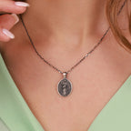 Silver necklace with a Mary Undoer of Knots pendant worn by a person against a light green background