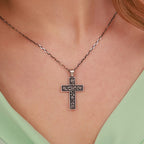 A close-up of a person wearing a sterling silver cross pendant necklace with an engraved rose branch design, styled with a light green top.