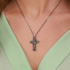 An oxidized sterling silver resurrection cross pendant necklace on a person wearing a light green top.