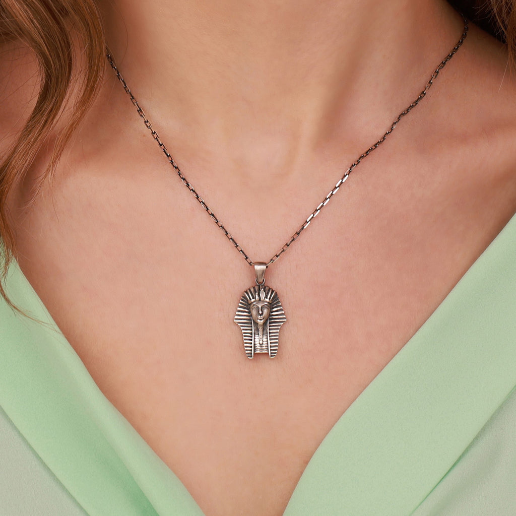 Necklace with a Pharaoh head pendant worn by a person in a green top.