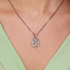 Necklace with a circular Virgin Mary pendant worn by a person against a light green background