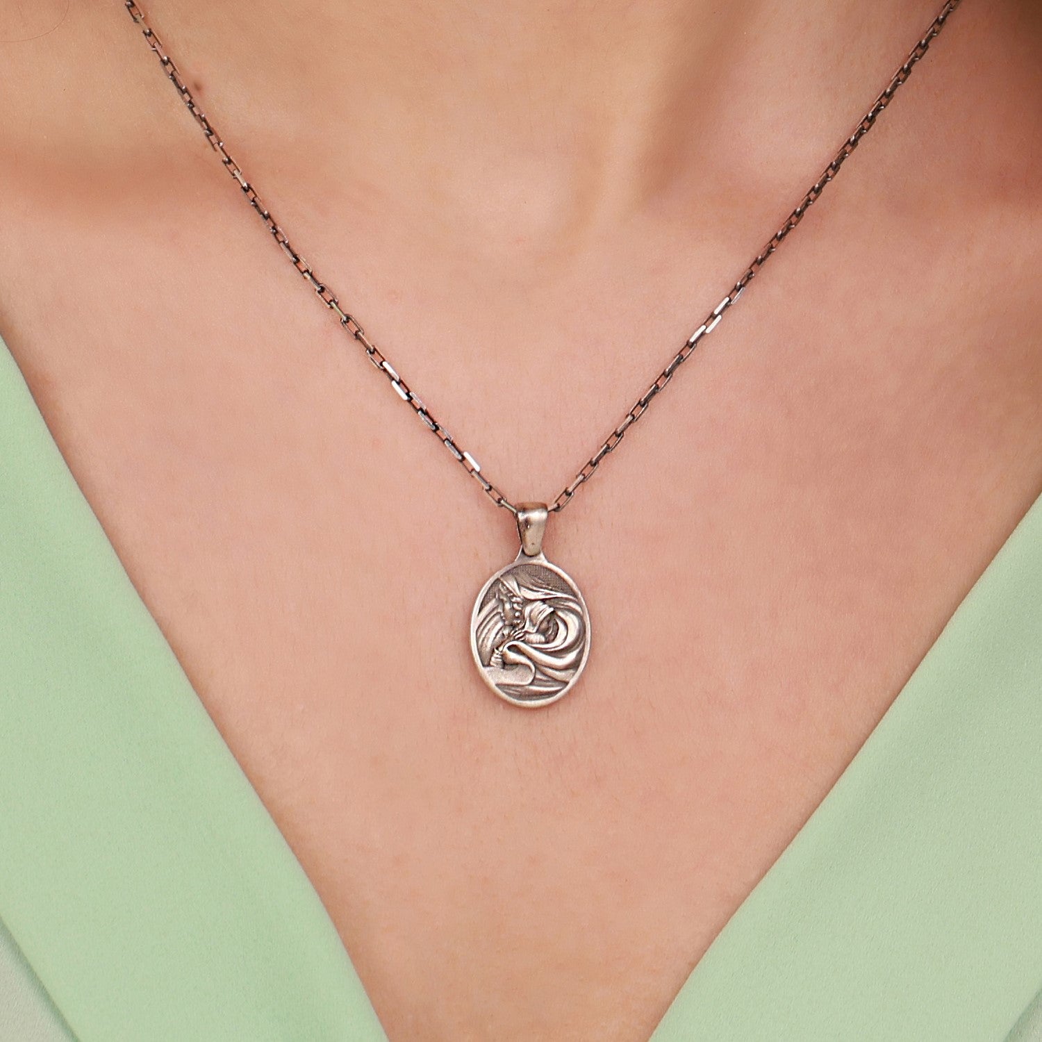 Necklace with a circular Virgin Mary pendant worn by a person against a light green background