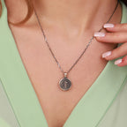 Necklace with a st benedict pendant worn by a person against a light green background