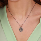 Silver necklace with an Our Lady of Charity pendant, worn by a person in a light green top.