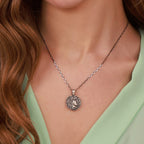 Silver necklace with a coin pendant worn by a person with wavy hair and a green top.