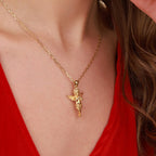 A gold necklace with a detailed cherub pendant worn by a model in a red top, shown in a close-up shot.