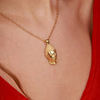 A gold pendant necklace featuring a Buddha head design, worn on a model's neck against a red top.