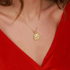 Gold necklace with a coin pendant worn by a person in a red top