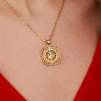 A gold pendant necklace with an ornate filigree border and a central North Star design, shown worn on a person's neck over a red top.