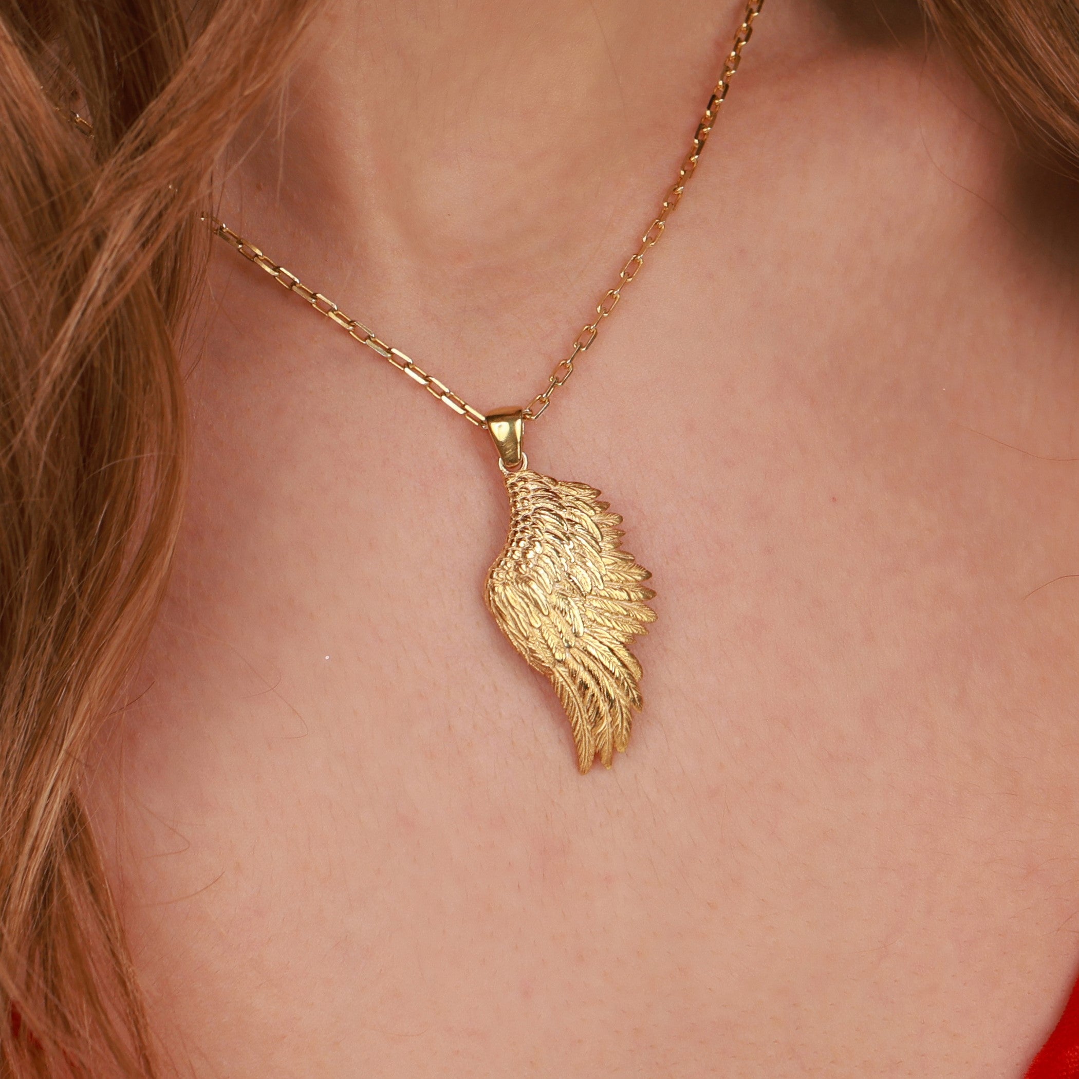 A gold angel wing-shaped pendant necklace worn on a model's neck, shown in a close-up shot with the model's skin and hair visible.