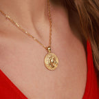 Gold necklace with a horse pendant in coin design worn by a person in a red outfit.