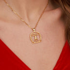A gold chain necklace with a Vitruvian Man pendant worn by a model in a red top.