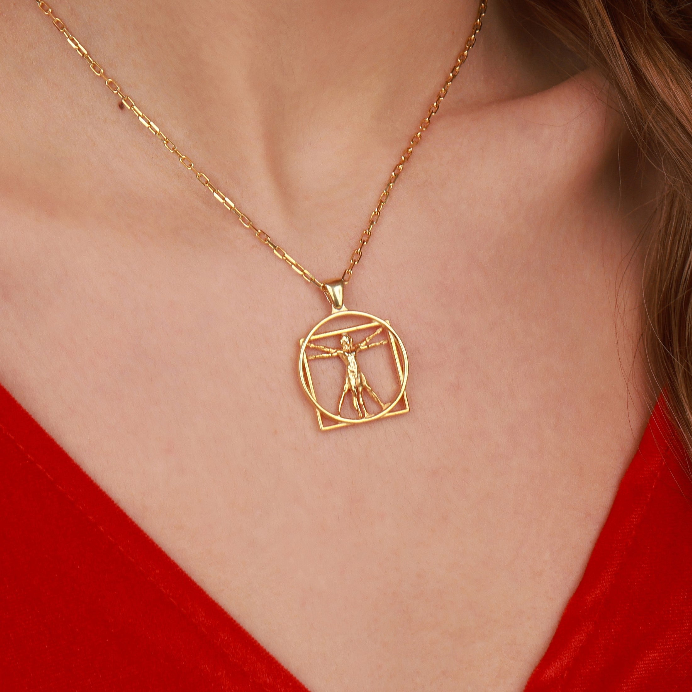 A gold chain necklace with a Vitruvian Man pendant worn by a model in a red top.