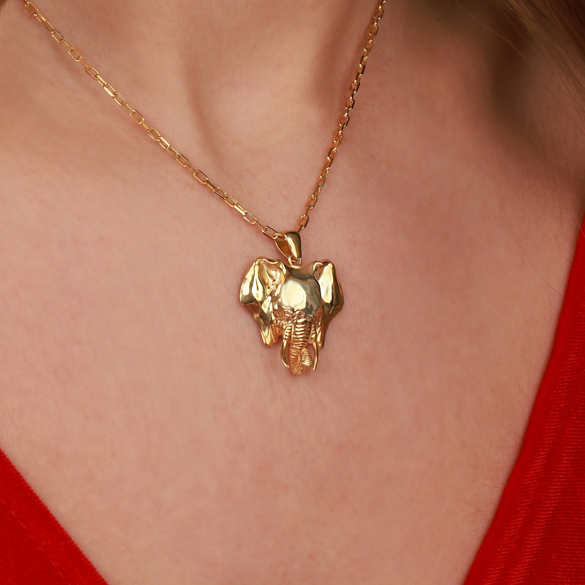 Gold elephant pendant necklace on a person wearing a red top
