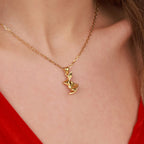 A gold necklace with an origami rabbit pendant worn by a person against a red garment.