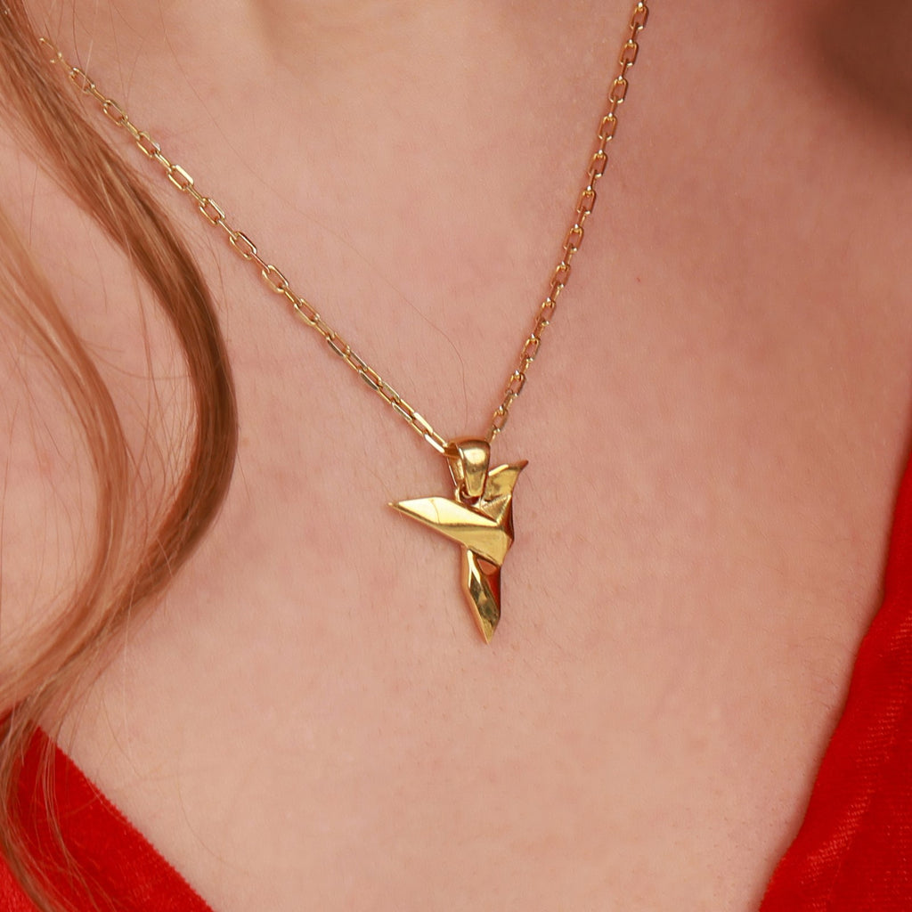 A gold necklace with a unique hummingbird pendant on a person wearing a red top.