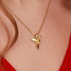 A gold necklace with a unique hummingbird pendant on a person wearing a red top.