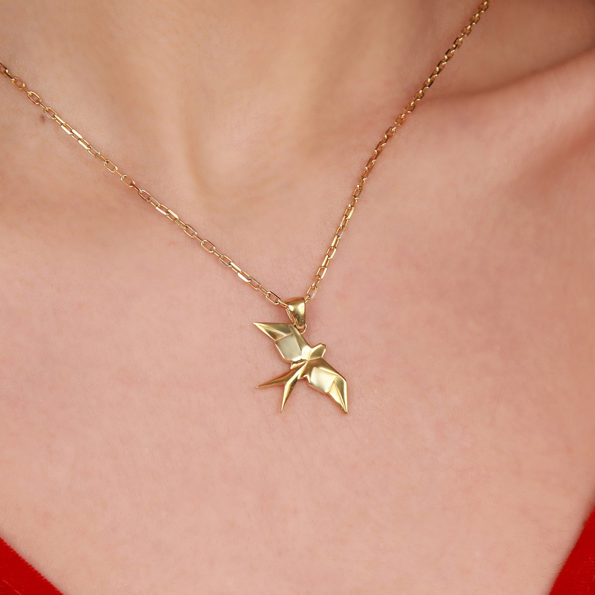 A gold necklace with a swallow-shaped pendant on a person's neck
