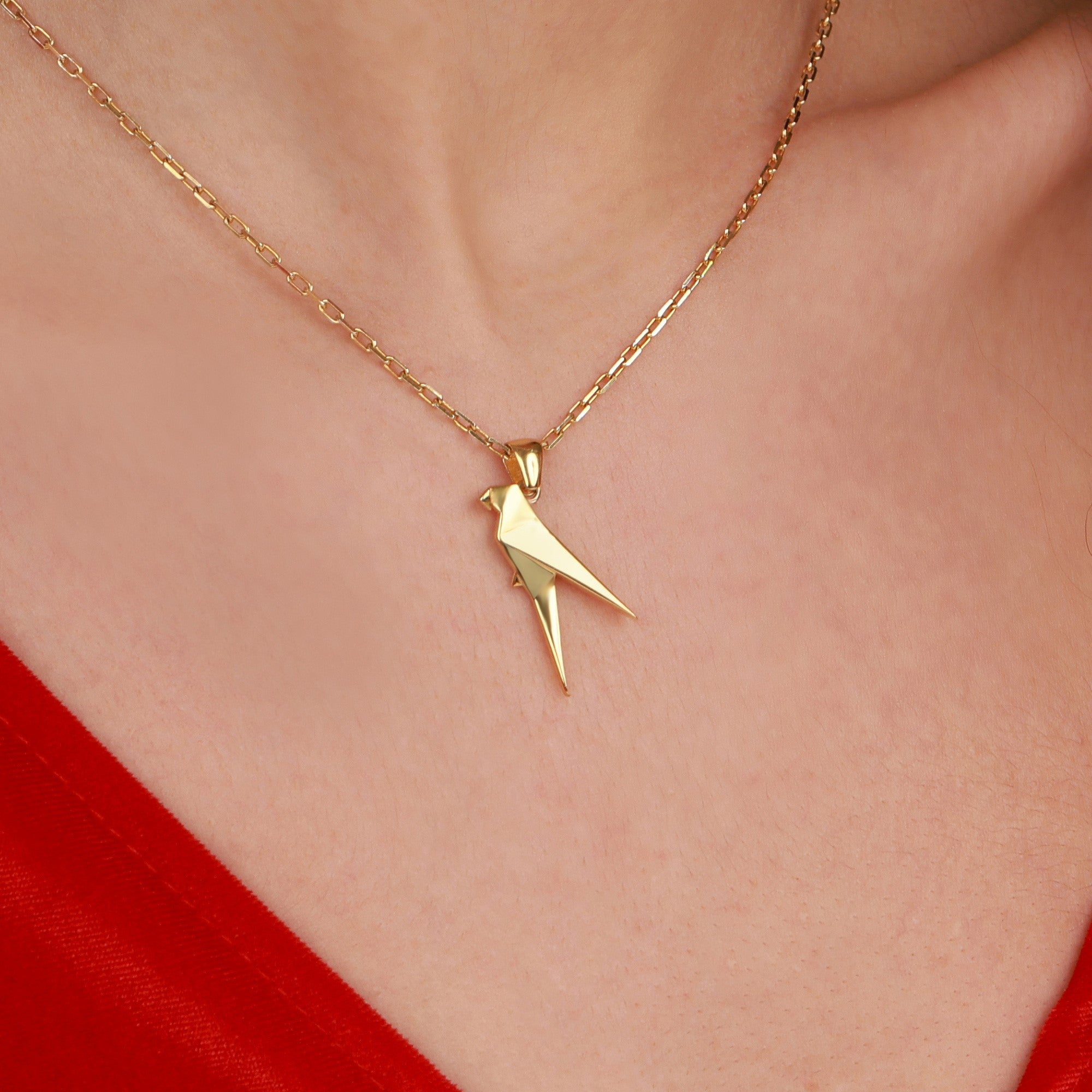 A gold necklace with a parrot-shaped pendant on a person wearing a red garment.
