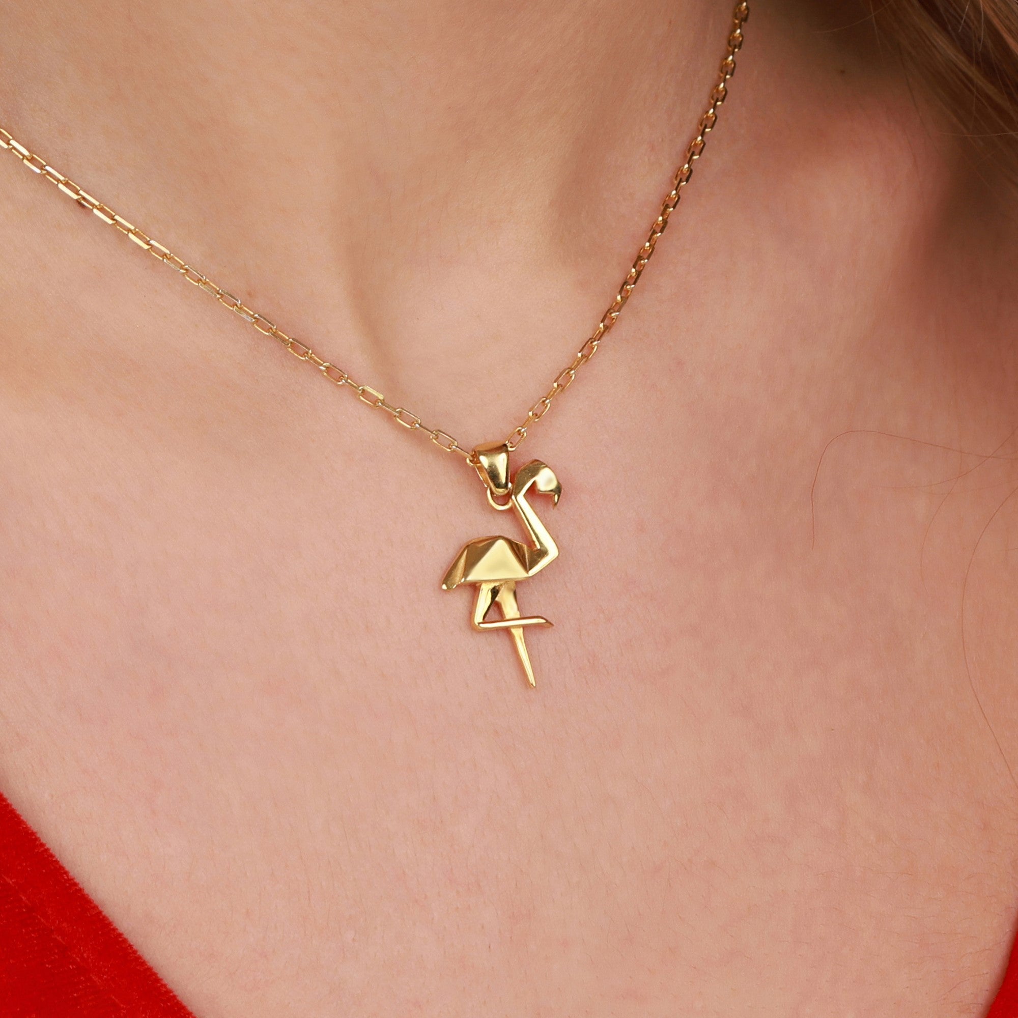 Gold flamingo pendant necklace on a person wearing a red top.
