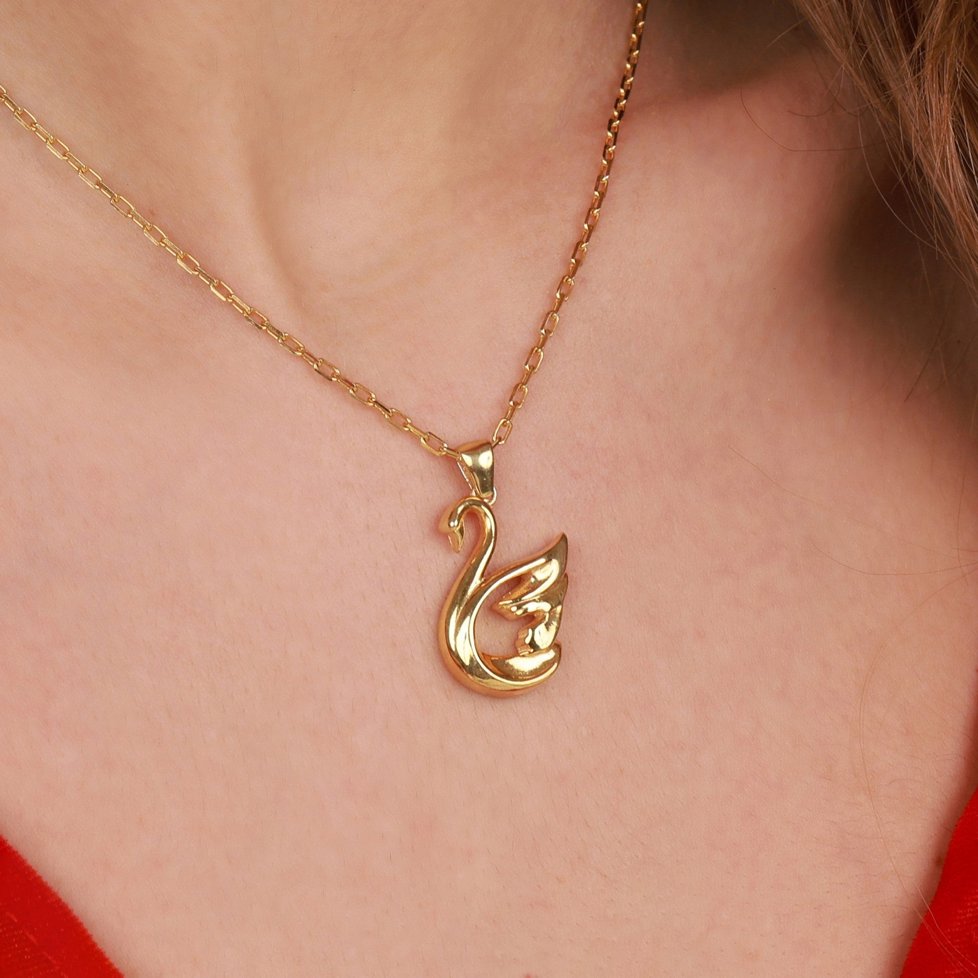 Gold swan pendant necklace on a person wearing a red top