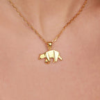 Gold bear pendant necklace on a person's neck against a pink background