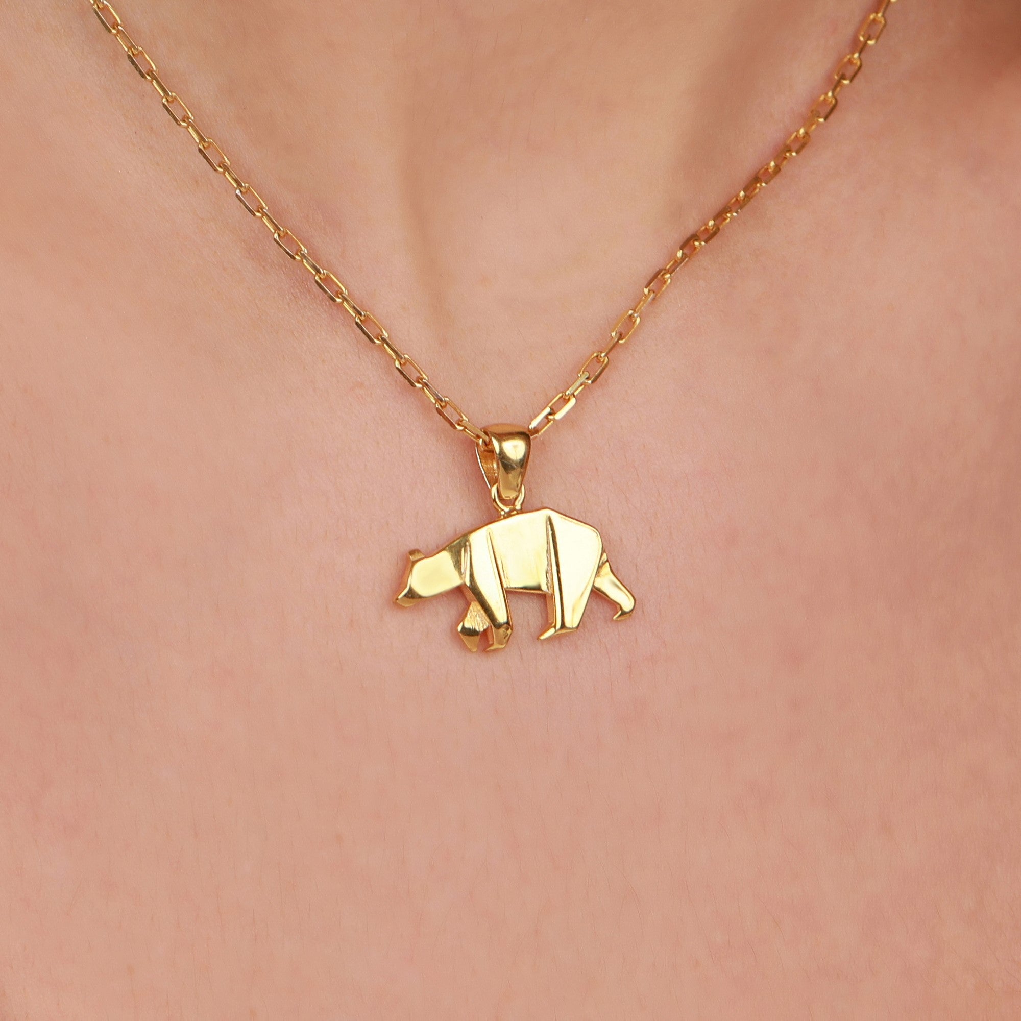 Gold bear pendant necklace on a person's neck against a pink background