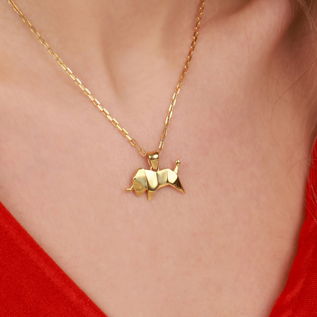 A gold necklace with a Taurus bull pendant on a person wearing a red top.