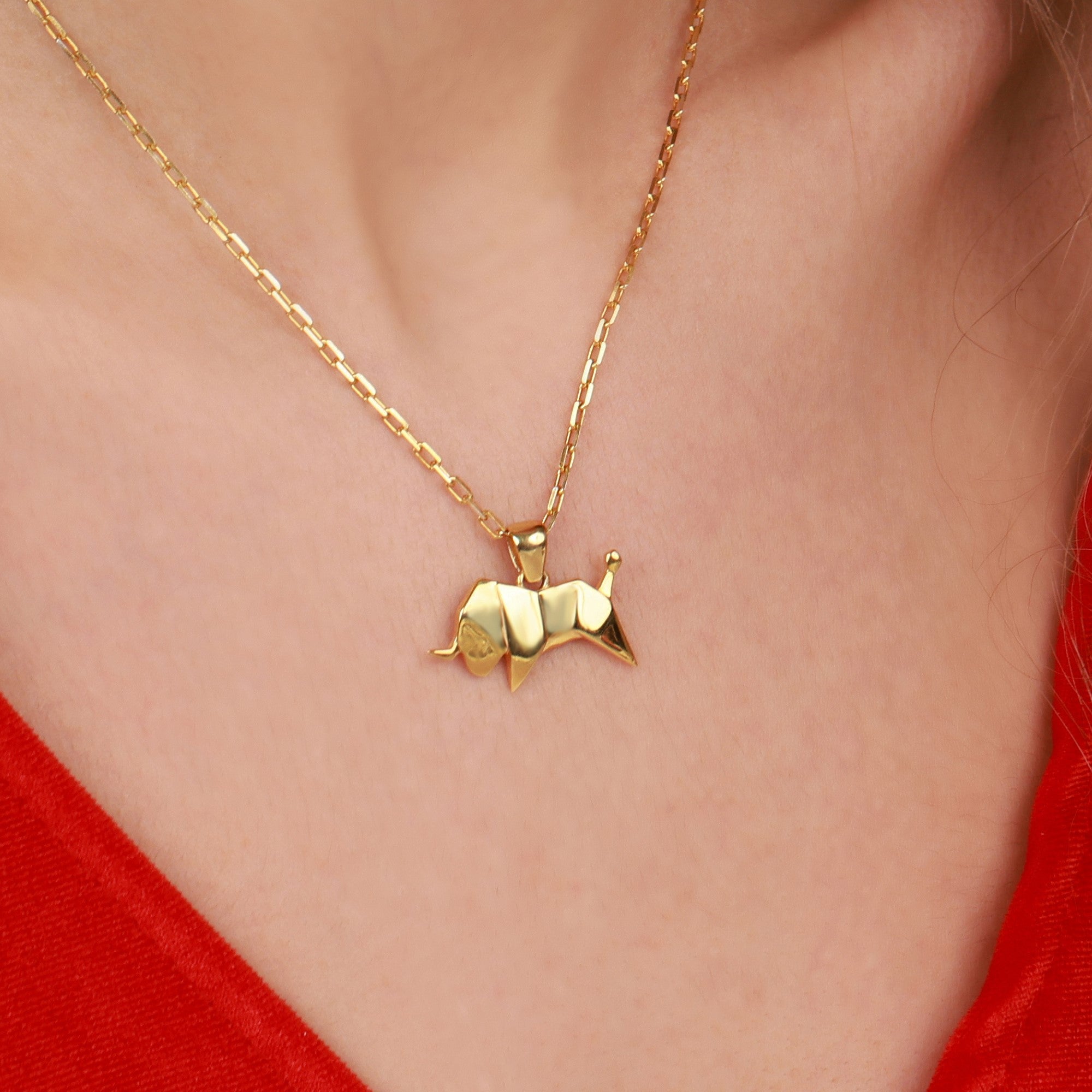 A gold necklace with a Taurus bull pendant on a person wearing a red top.