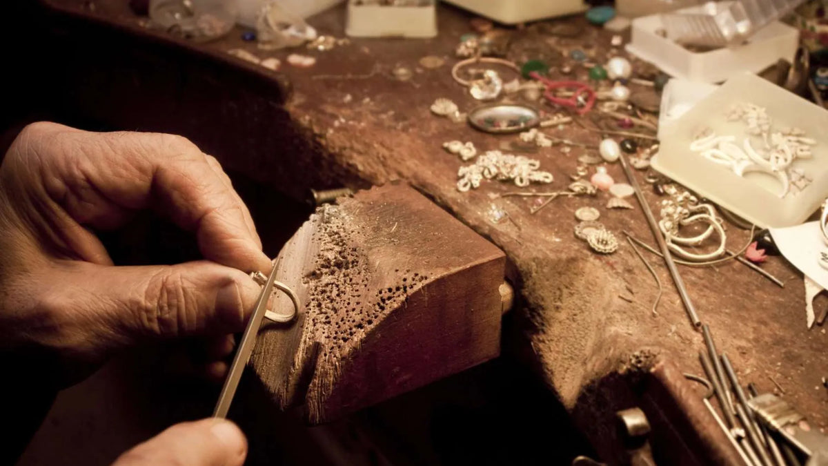 Jeweler working on a piece of jewelry with tools and materials on a workbench.