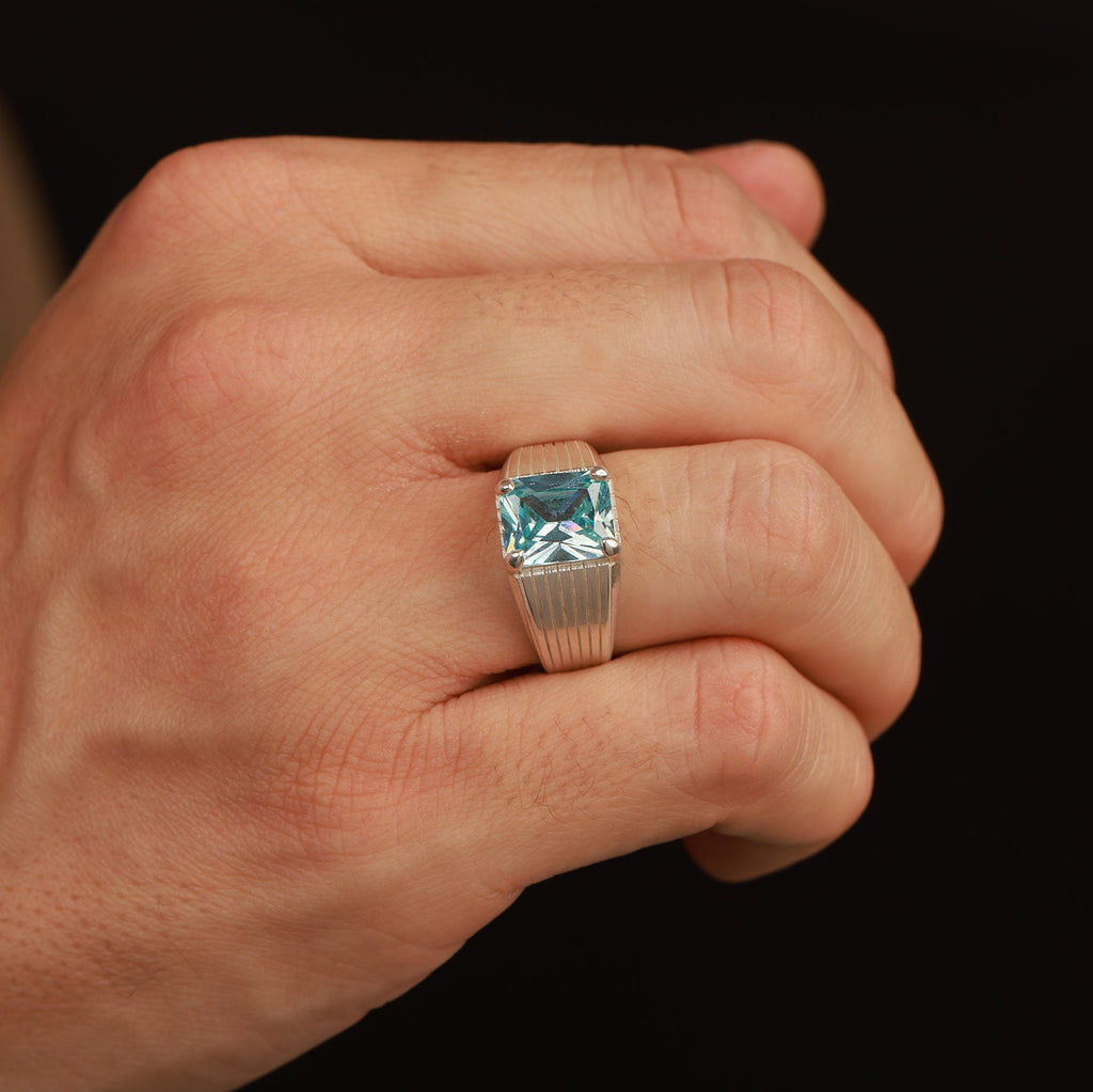 Hand wearing a ring with a blue gemstone on a black background