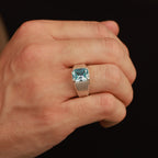 Hand wearing a ring with a blue gemstone on a black background
