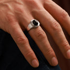 Hand wearing a silver ring with a black stone on a blurred background