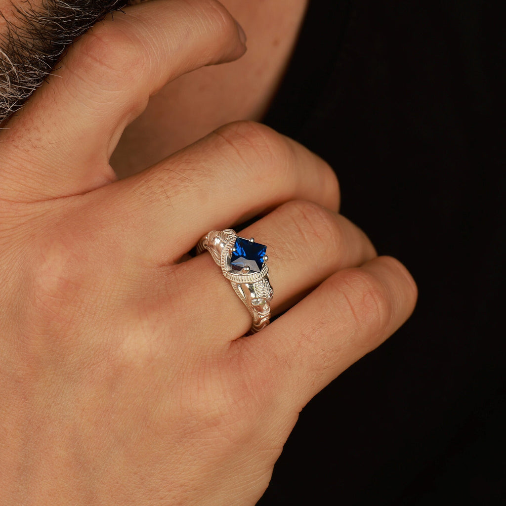 Hand wearing a polished silver ring with a blue gemstone against a dark background
