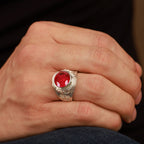 Hand wearing a silver ring with a red gemstone signet ring on a blurred background